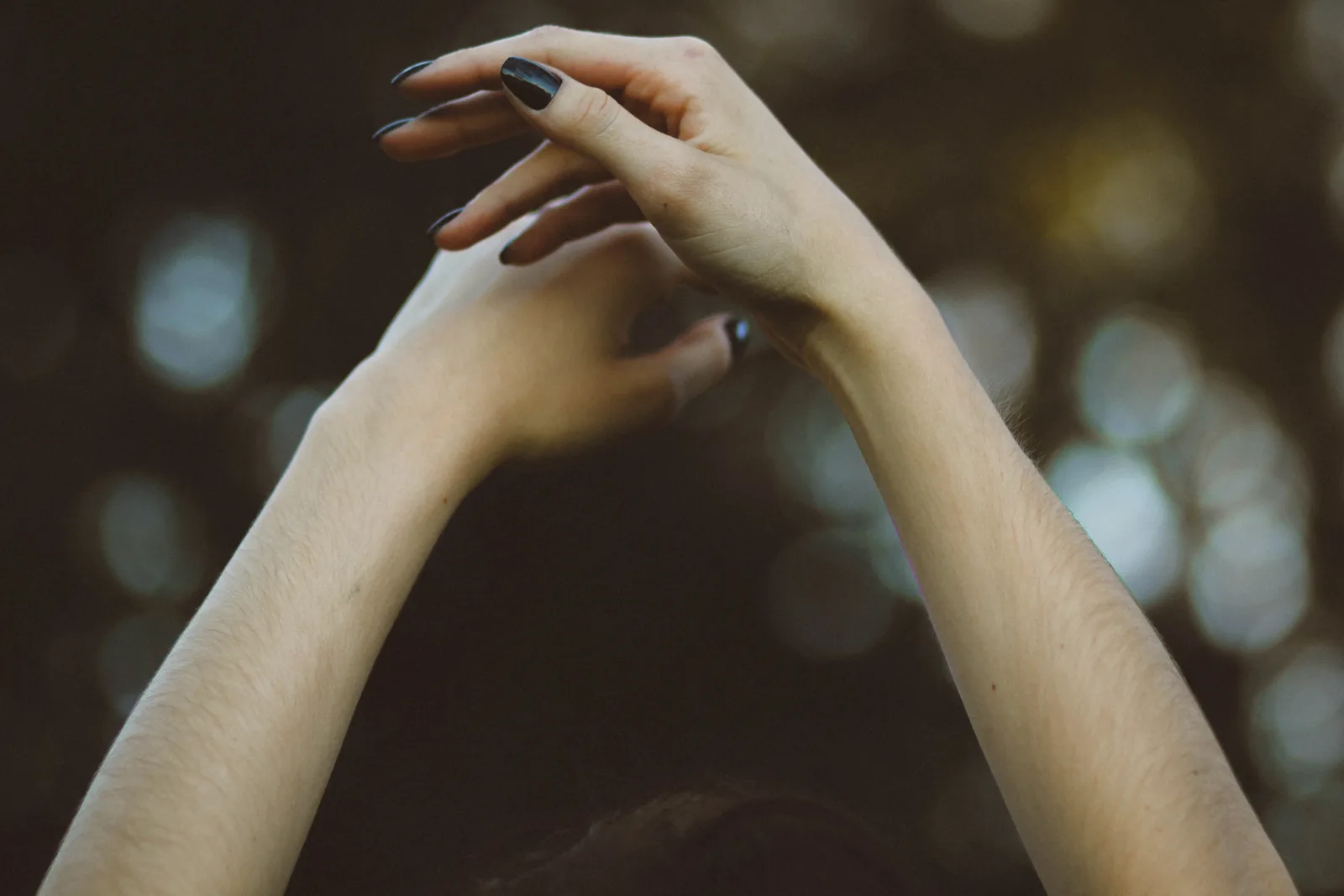 Two hands with dark polished nails held up against soft lights
