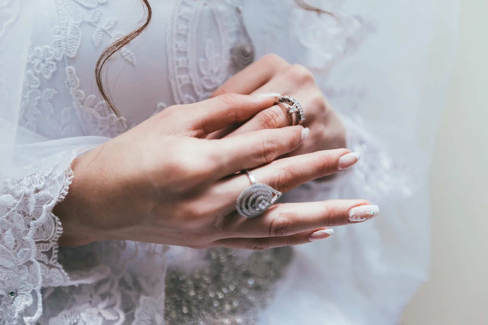 Hands with pale nails and rings folded over white lace